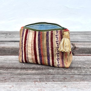 Può includere: Un astuccio rettangolare aperto con un motivo a righe beige, rosse, viola e arancioni. Ha una cerniera verde e un nappa dorata. L'interno è in tessuto azzurro. L'astuccio è realizzato in materiale tessuto.