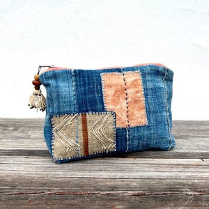 Könnte beinhalten: Eine blaue Denim-Tasche mit dekorativen Aufnähern in Beige und Braun. Die Tasche hat einen Reißverschluss mit Quasten- und Holzperlen-Detail. Die Aufnäher weisen gestickte Designs und einen vertikalen Streifen auf.