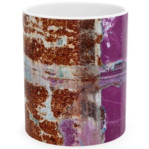 May include: A white ceramic mug with a wrap-around design featuring a distressed, textured pattern. The design incorporates shades of brown, purple, and blue, creating a weathered, industrial aesthetic. The mug is cylindrical and suitable for hot or cold beverages.