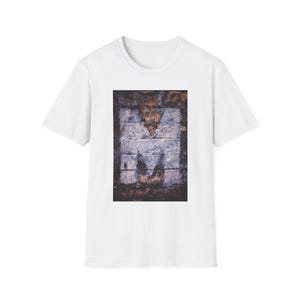 May include: White t-shirt with a graphic of a white letter "M" painted on a brick wall.