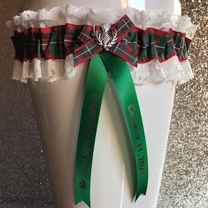 May include: White lace garter with a red and green tartan ribbon and a silver thistle charm. The ribbon has the text "Mr. & Mrs. McCall" and "October 31, 2021" printed on it.