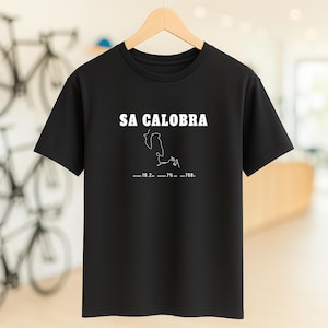 Puede incluir: Camiseta negra de cuello redondo con el texto blanco "SA CALOBRA" sobre un dibujo lineal blanco de una carretera. Debajo del dibujo están los números "10.2... 7%... 708."