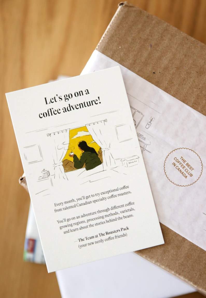Pu&ograve; includere: Un biglietto bianco con un'illustrazione disegnata a mano di una persona che guarda fuori da una finestra mentre tiene una tazza di caff&egrave;. Il testo sul biglietto dice "Let's go on a coffee adventure!" e "Ogni mese, potrai provare un caff&egrave; eccezionale di torrefattori canadesi specializzati. Ti imbarcherai in un'avventura attraverso diverse regioni di coltivazione del caff&egrave;, metodi di lavorazione, variet&agrave; e imparerai le storie dietro i chicchi. - Il team di The Roasters Pack (i tuoi nuovi amici del caff&egrave;)"