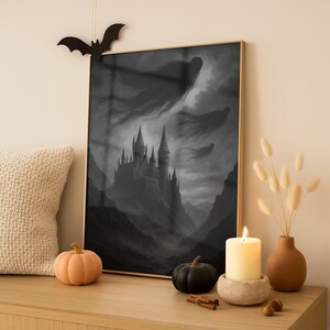 May include: A framed grayscale print of a castle on a mountain, with ghostly figures in the sky. A black bat decoration hangs above the frame. Decorative pumpkins, a lit candle, and a vase with dried flowers sit on a wooden surface.