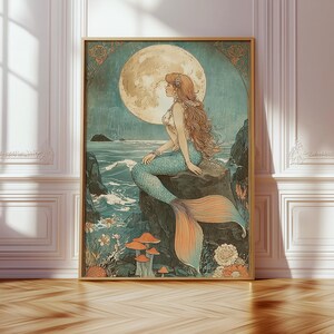 May include: A framed art print featuring a mermaid sitting on a rock, gazing at a full moon. The mermaid has long auburn hair and a turquoise tail. The artwork has a vintage style with muted colors and floral accents.