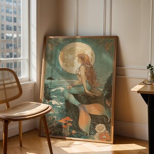 May include: A framed art print featuring a mermaid sitting on a rock, with a full moon in the background. The mermaid has long red hair and a teal tail. The artwork has a vintage, art nouveau style.