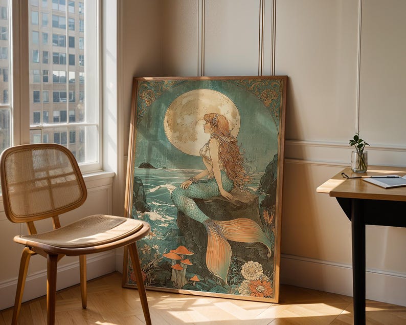 May include: A framed art print featuring a mermaid sitting on a rock, with a full moon in the background. The mermaid has long red hair and a teal tail. The artwork has a vintage, art nouveau style.