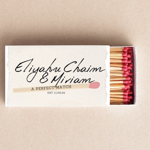 Puede incluir: Una caja de cerillas blanca con el texto "Eliyahu Chaim & Miriam A PERFECT MATCH EST 11.06.24" y una sola cerilla con una cabeza rosa que sobresale de la caja.