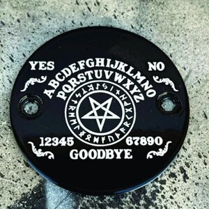 Pu&ograve; includere: Una planchette Ouija nera e circolare con lettere e simboli bianchi. La planchette presenta l'alfabeto, i numeri e le parole "YES", "NO" e "GOODBYE". Una stella a cinque punte &egrave; al centro.