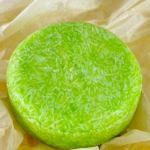 Könnte beinhalten: Eine runde, grüne Shampoo-Seife mit weißen Flecken. Die Seife liegt auf einem Stück braunem Papier.