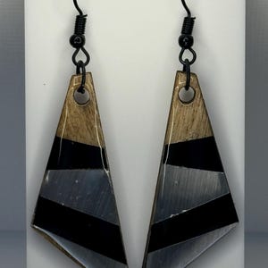 May include: A pair of triangle-shaped earrings with black and brown stripes. The earrings are made of wood and resin and have a silver-colored finish.