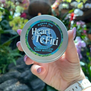May include: A silver tin of Madam Mim Wicked Skin body butter labelled "Heart of Te Fiti Coconut & Marshmallow Body Butter".
