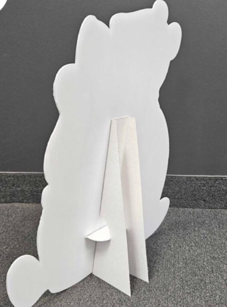 Peut inclure: D&eacute;coupe en carton blanc en forme d'ours, vue de dos. La d&eacute;coupe est soutenue par un support &agrave; l'arri&egrave;re, lui permettant de tenir debout. La forme d'ours a des bords arrondis et un design simple.