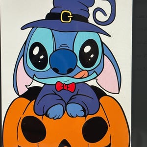 May include: A cartoon character, in blue, wearing a witch hat and bow tie, sits atop an orange jack-o'-lantern. The character has large black eyes, a pink tongue, and pointed ears. The witch hat is dark blue with a gold buckle.