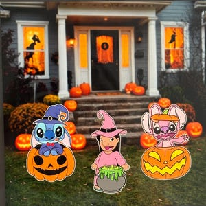 May include: Halloween yard decorations featuring characters in witch hats and pumpkins. The decorations include a blue alien character, a girl holding a cauldron, and a pink alien character. The background shows a house decorated for Halloween with pumpkins and orange lighting.