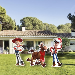 May include: Cardboard cutouts of Jessie, Bullseye, and Woody from Toy Story stand on a green lawn in front of a house. Jessie wears a red hat, white shirt, and cow-print trousers. Woody wears a cowboy hat and vest. Bullseye has a red scarf.