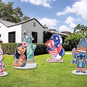 Op de afbeelding: Tuindecoraties met stripfiguren en patriottische thema's. Inclusief een roze personage met ballonnen, een meisje, het Vrijheidsbeeld, een ballonnenarrangement en een personage met een "Aloha" surfplankhoed. De decoraties staan op een groen gazon.