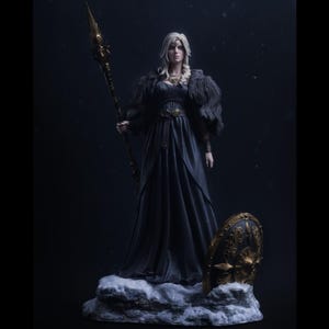 May include: A detailed statue of a woman in a dark blue gown, holding a golden spear. She has long blonde hair and a fur shawl. A golden shield rests on a snowy base. The statue has intricate details and a regal appearance.