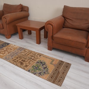 May include: A rectangular, patterned rug with a brown, beige, and blue color scheme. The rug is placed in front of two brown leather armchairs and a small wooden table. The rug's design features geometric and floral motifs.