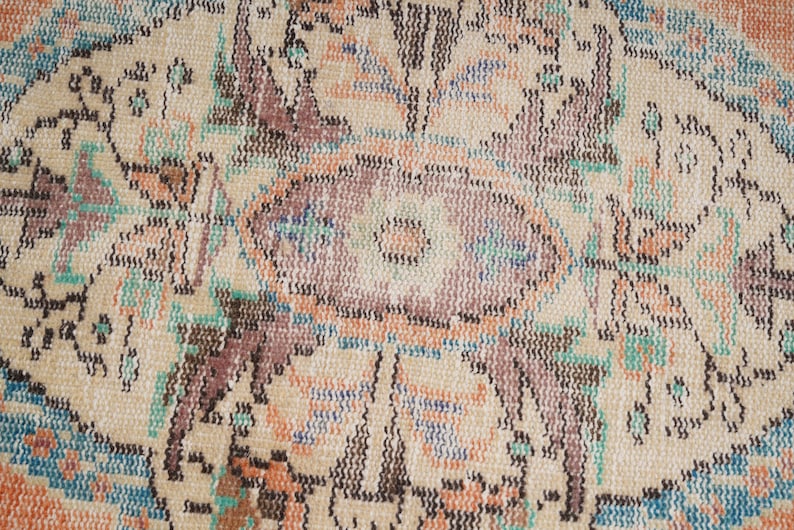 Pode incluir: Close-up de um tapete bege com um padr&atilde;o floral em tons de marrom, azul e rosa. O tapete tem uma textura tecida e um design detalhado.
