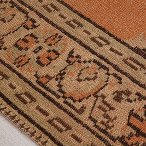 May include: Close-up of a section of a vintage rug. The rug features a warm color palette with shades of orange, brown, and beige. Intricate geometric patterns and borders are visible, showcasing a traditional design.