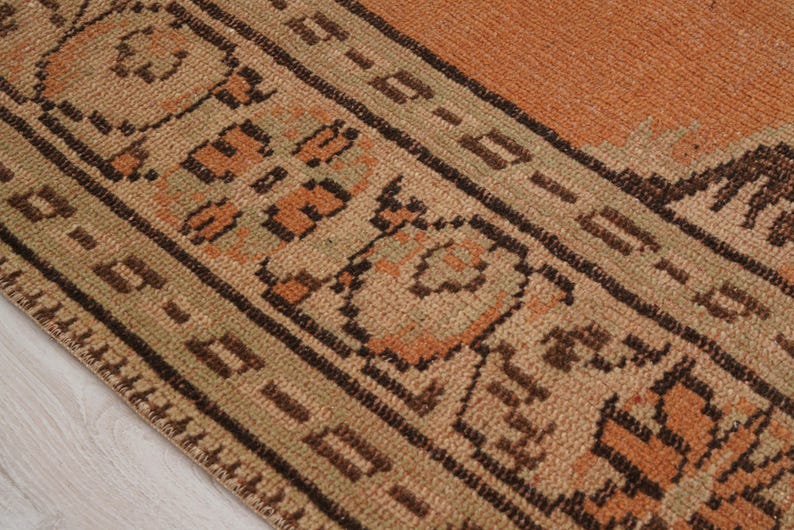 May include: Close-up of a section of a vintage rug. The rug features a warm color palette with shades of orange, brown, and beige. Intricate geometric patterns and borders are visible, showcasing a traditional design.