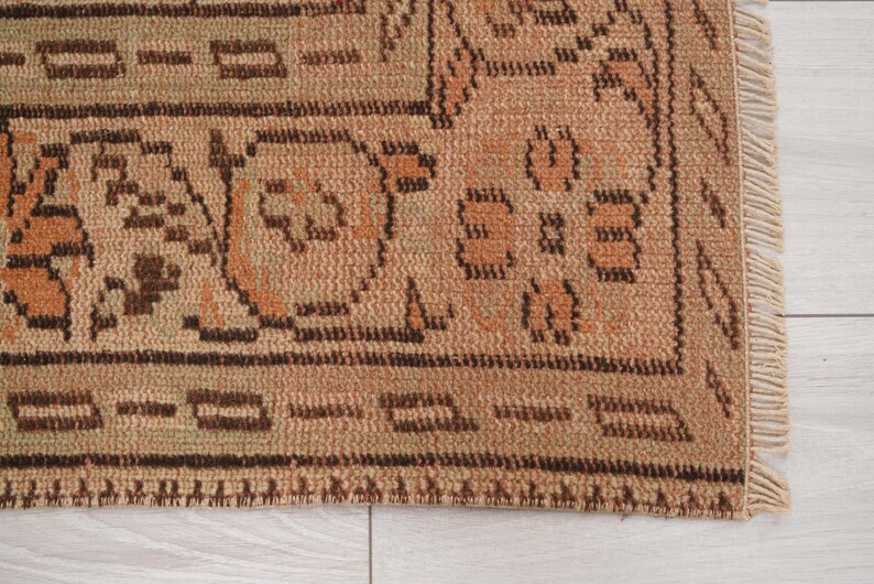 May include: Close-up of a section of a beige and brown patterned rug. The rug features geometric and floral designs in shades of brown and orange. The edge of the rug has a fringe.