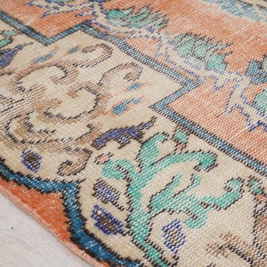 Pode incluir: Um tapete vintage com fundo creme e borda p&ecirc;ssego. O tapete tem um padr&atilde;o floral em tons de azul, verde e marrom.