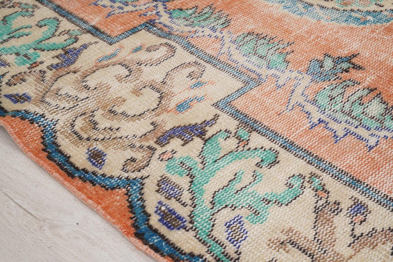 Pode incluir: Um tapete vintage com fundo creme e borda p&ecirc;ssego. O tapete tem um padr&atilde;o floral em tons de azul, verde e marrom.