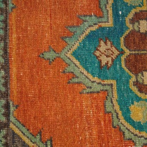 May include: Close-up of a section of a vintage rug with a detailed geometric pattern. The rug features a vibrant color palette of orange, teal, brown, and green. The design includes stylized floral and geometric shapes, creating a textured, antique aesthetic.