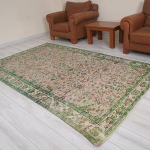 May include: A vintage rug with a beige background and a green border. The rug has a floral pattern with shades of brown, green, and beige.
