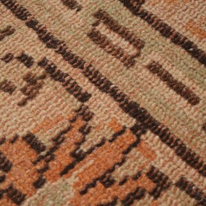 May include: Close-up of a woven rug with a geometric pattern. The rug features a blend of beige, brown, and orange hues. Diagonal lines and rectangular shapes create the design, offering a textured appearance.
