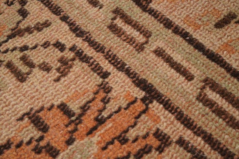 May include: Close-up of a woven rug with a geometric pattern. The rug features a blend of beige, brown, and orange hues. Diagonal lines and rectangular shapes create the design, offering a textured appearance.