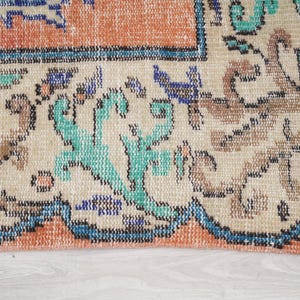 Pode incluir: Close-up da borda inferior de um tapete com fundo creme e um padr&atilde;o floral colorido. O tapete tem uma borda azul com uma borda interior cor de p&ecirc;ssego.