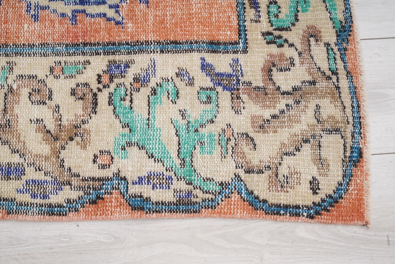 Pode incluir: Close-up da borda inferior de um tapete com fundo creme e um padr&atilde;o floral colorido. O tapete tem uma borda azul com uma borda interior cor de p&ecirc;ssego.