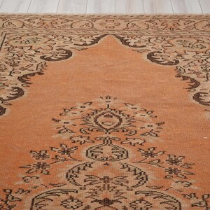 May include: An antique rug with a warm orange field and intricate dark brown floral and geometric patterns. The rug features a detailed border and a central medallion design, showcasing traditional craftsmanship.