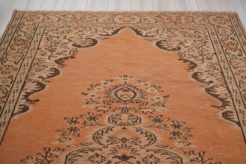 May include: An antique rug with a warm orange field and intricate dark brown floral and geometric patterns. The rug features a detailed border and a central medallion design, showcasing traditional craftsmanship.