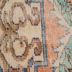 Pode incluir: Close-up de um tapete bege com um padr&atilde;o geom&eacute;trico colorido. O tapete tem uma borda de franja e apresenta tons de marrom, azul, verde e laranja.