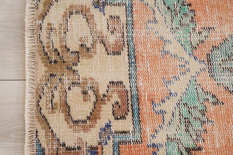 Pode incluir: Close-up de um tapete bege com um padr&atilde;o geom&eacute;trico colorido. O tapete tem uma borda de franja e apresenta tons de marrom, azul, verde e laranja.