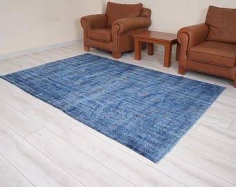 May include: A blue distressed rug with a faded pattern. The rug is laid out on a light wood floor in a room with two brown leather armchairs and a wooden coffee table.