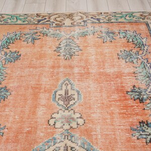 Pode incluir: Um tapete vintage com fundo cor de p&ecirc;ssego e um padr&atilde;o floral em tons de azul, verde e creme. O tapete tem um aspeto desgastado e uma textura desgastada.
