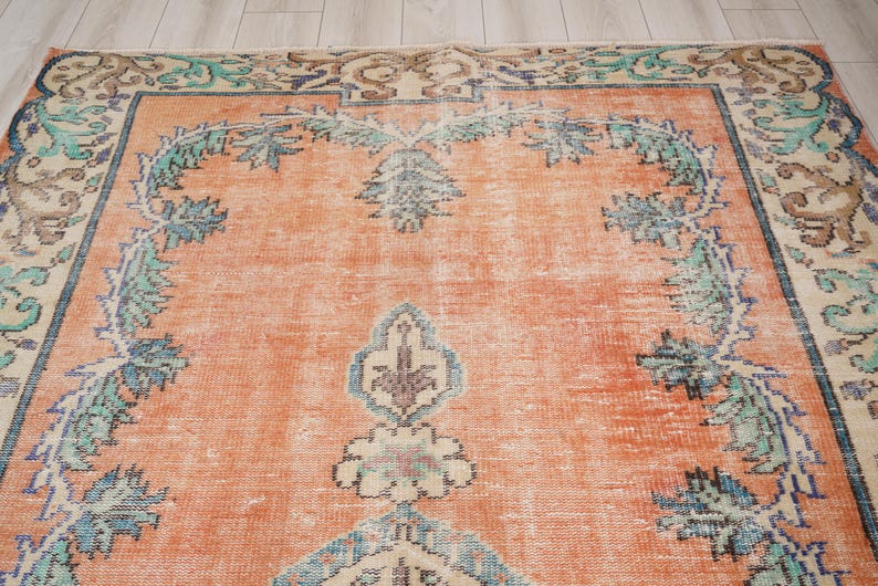 Pode incluir: Um tapete vintage com fundo cor de p&ecirc;ssego e um padr&atilde;o floral em tons de azul, verde e creme. O tapete tem um aspeto desgastado e uma textura desgastada.