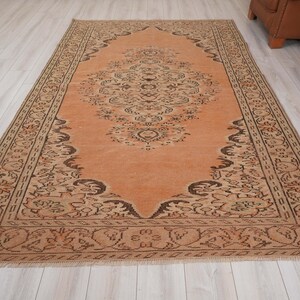 May include: A rectangular, vintage-style rug with an intricate floral pattern in shades of peach and brown. The rug features a central medallion design and a detailed border. The rug is placed on a light-colored wooden floor, showcasing its warm tones and traditional aesthetic.