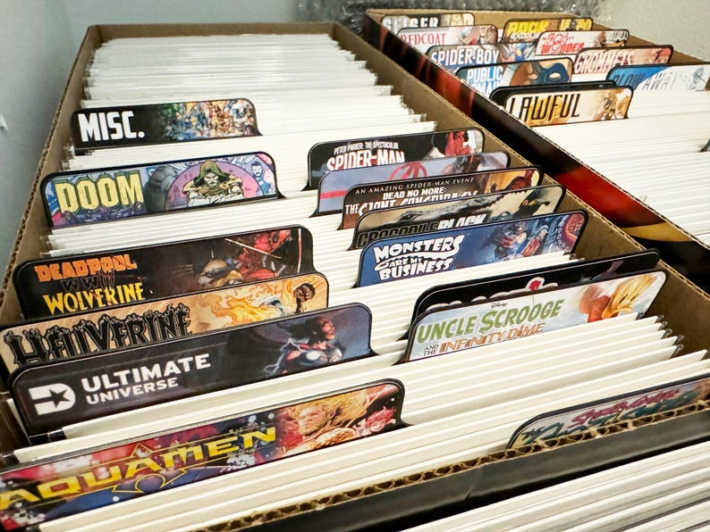 Peut inclure: Gros plan sur une bo&icirc;te remplie de bandes dessin&eacute;es. La bo&icirc;te est divis&eacute;e en sections avec des &eacute;tiquettes pour diff&eacute;rentes cat&eacute;gories de bandes dessin&eacute;es, notamment "MISC.", "DOOM", "DEADPOOL VS WOLVERINE", "ULTIMATE UNIVERSE", "AQUAMEN", "SPIDER-MAN", "CROCODILE  DAVE", "MONSTERS  CART  WI BUSINESS", "UNCLE SCROOGE AND THE INFINITY DIME", "REDCOAT", "SPIDER BOY PUBLIC", "LAWFUL", et plus.