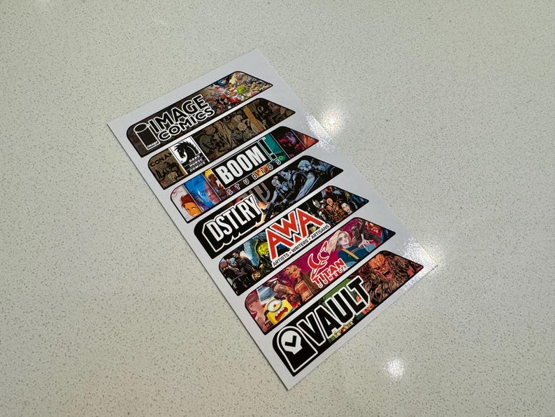 Peut inclure: Un ensemble de sept autocollants color&eacute;s repr&eacute;sentant les logos de diff&eacute;rents &eacute;diteurs de bandes dessin&eacute;es, dont Image Comics, Boom! Studios, AWA et Vault Comics.