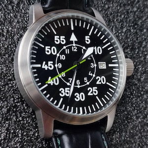 Puede incluir: Un reloj de pulsera de acero inoxidable con esfera negra y números blancos. El reloj tiene un segundero verde y una correa de cuero negro. La esfera muestra la hora y la fecha.