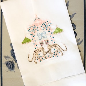 Op de afbeelding: Witte handdoek met geborduurde roze en groene pagode met twee luipaarden en het monogram "JC" in blauw.