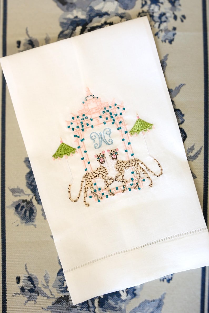 Op de afbeelding: Witte handdoek met geborduurde roze en groene pagode met twee luipaarden en het monogram "JC" in blauw.