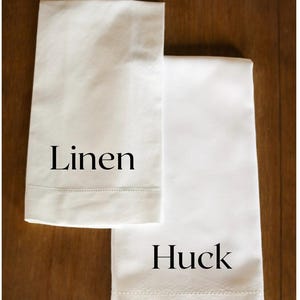 K&ouml;nnte beinhalten: Zwei wei&szlig;e K&uuml;chent&uuml;cher, eines mit der Aufschrift "Leinen" und das andere mit der Aufschrift "Huck".
