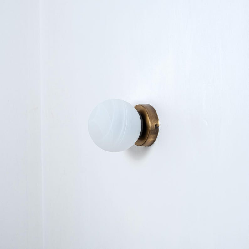 May include: A brass wall sconce with a white frosted glass globe shade.